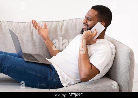 Black man talking on smartphone while lying on sofa in living room at home Stock Photo