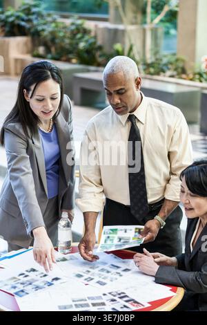 Middle-aged Black businessman reviewing documents with Asian and mixed-race female colleagues standing at table during meeting outdoors Stock Photo