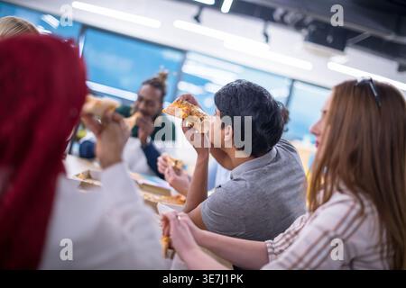Diverse group of business people eating pizza together while sitting at table and enjoying lunchtime break in the office Stock Photo