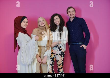 Middle Eastern women in traditional Muslim clothing standing with male and female friends against pink background in studio Stock Photo
