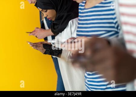 Cheerful diverse group of friends using their smartphones while standing against colorful wall in studio Stock Photo