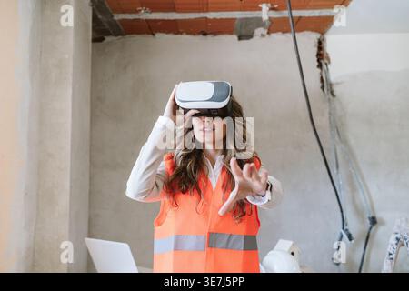Hispanic female architect using VR headset reaching hand forward standing in construction site during daytime Stock Photo