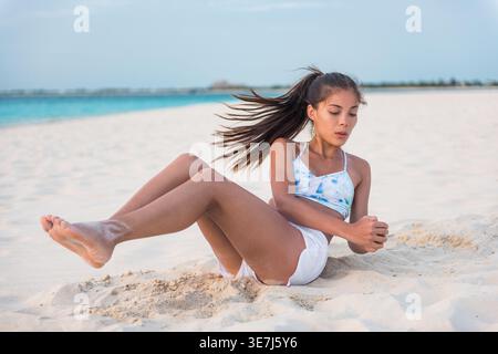 Asian woman doing Russian twists abs exercises with raised legs at the beach Stock Photo