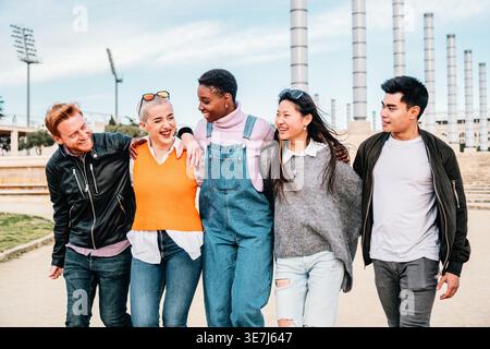 Cheerful group of diverse male and female friends walking together on city street during daytime Stock Photo