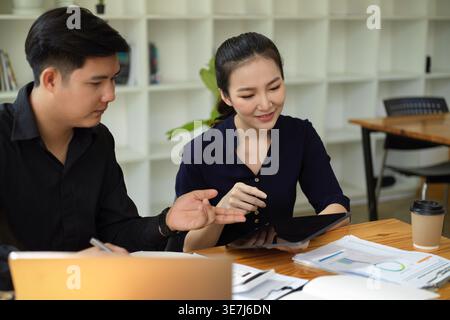 Asian male and female colleagues sitting at table working together in office Stock Photo