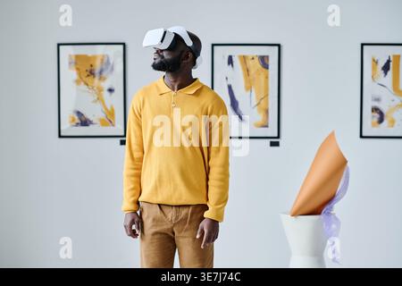 Black man wearing VR headset experiencing virtual reality while standing in art gallery Stock Photo