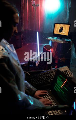 Mixed race woman using laptop with Black man looking away with lights on head sitting on floor in dark room Stock Photo