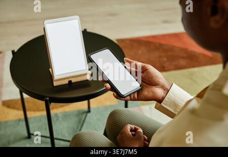 Black woman connecting smartphone to smart home screen control system sitting on chair indoors Stock Photo
