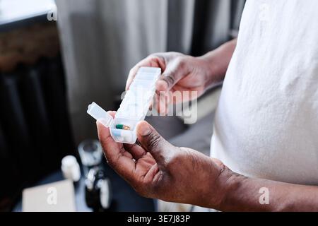 Hands of Black senior man holding plastic container with medicine while standing at home Stock Photo