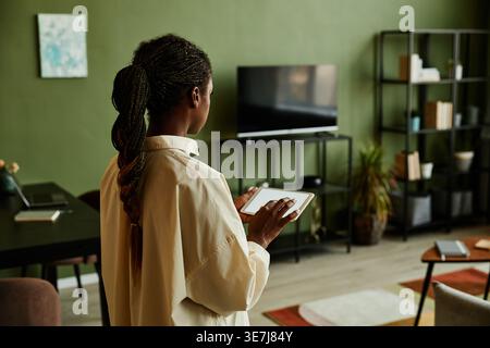 Black woman holding tablet with blank screen while operating smart home devices standing in living room at home Stock Photo