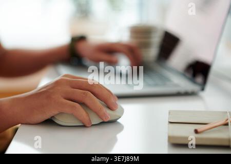 Asian male office worker using mouse working on laptop sitting at desk in office Stock Photo
