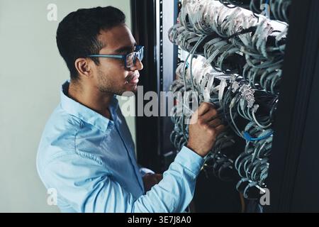 Man, IT technician and checking cables in mainframe for troubleshooting, storage or connection. Male person, employee or network engineer with working Stock Photo