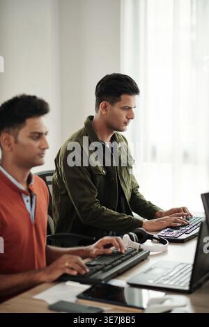Indian male programmers typing on computer keyboards while sitting at desk in office Stock Photo