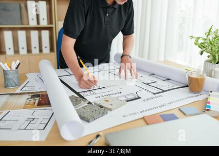 Asian male architect working on blueprint standing at drawing table in office Stock Photo