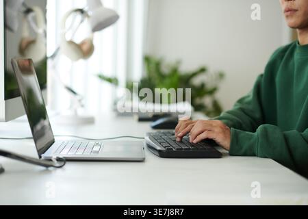 Asian male programmer typing codes on computer while sitting at table with laptop in office Stock Photo