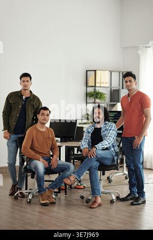 Serious group of Indian businessmen standing and sitting at table with computers in office Stock Photo