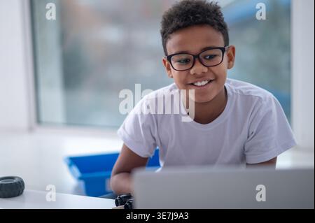 Smiling Black boy in eyeglasses using laptop while sitting at home Stock Photo