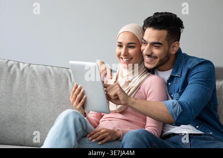 Smiling Middle Eastern couple using tablet while sitting on sofa at home Stock Photo