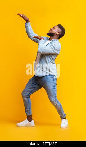 Black man having fun dancing against yellow background in studio Stock Photo