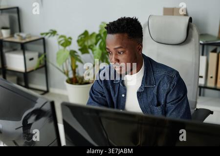 Serious Black man working on computer while sitting at table in office Stock Photo