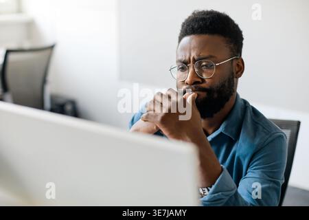 Thoughtful black man in eyeglasses stack with hard task, looking at computer screen, businessman thinking of problem solution, making difficult decisi Stock Photo