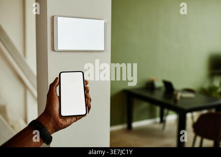 Black man using smartphone while connecting to smart home system standing indoors Stock Photo