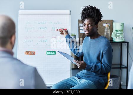 Black man with dreads writing on whiteboard during English lesson with group of people in office Stock Photo