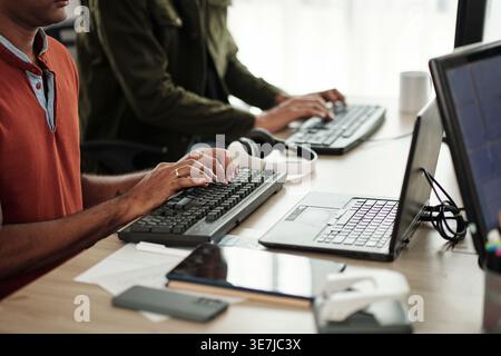 Indian male programmers typing on computer keyboards while sitting at desk in office Stock Photo