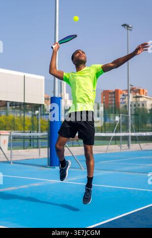 Black man playing pickleball jumping on outdoor court on sunny day Stock Photo