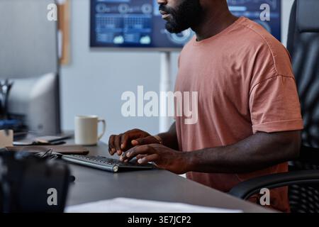 Cropped shot of Black male programmer typing codes on computer while sitting at table in office Stock Photo