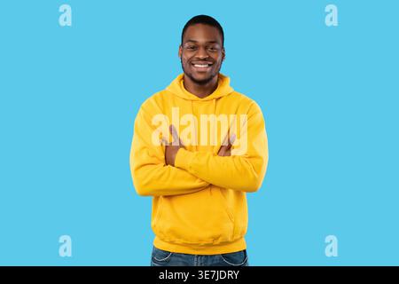 Smiling bearded Black man wearing hoodie standing with crossed arms in front of blue background in studio Stock Photo