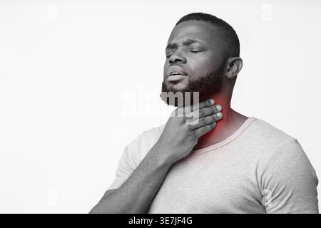 Black man suffering from sore throat touching neck while standing against white background in studio Stock Photo