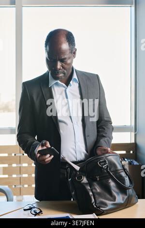 Black businessman using smLifestylephone standing at desk in office Stock Photo