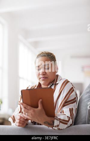 Vertical portrait of modern mixed-race woman holding digital tablet while using online app at home, copy space Stock Photo