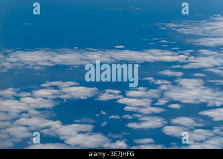 Aerial view looking down at scattered white cumulus clouds arranged in rows and clusters over the deep blue Pacific Ocean near New Zealand, shot from Stock Photo