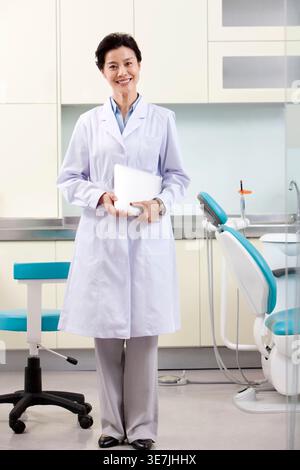 Smiling middle-aged Chinese female dentist holding tablet while standing in dental clinic Stock Photo