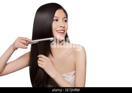Chinese woman looking away wrapped on bath towel while combing black long hair against white background in studio Stock Photo