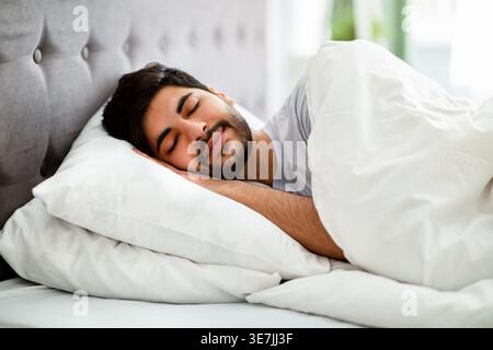 Arab man with beard sleeping on bed with white blanket in bedroom at home Stock Photo