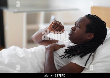 Black man with dreads coughing while lying on bed at home Stock Photo