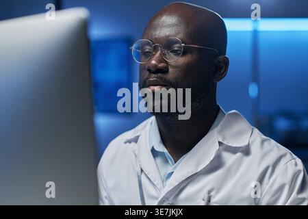 Black male computer engineer in eyeglasses looking at computer screen while sitting in laboratory Stock Photo