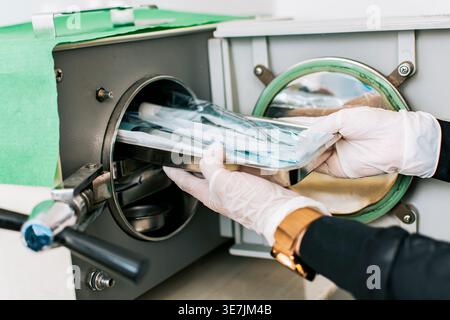 Hands of Nicaraguan female dentist wearing gloves sterilizing tools on dental autoclave in clinic Stock Photo