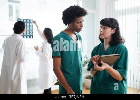 Black male and caucasian female nurses discussing data on tablet with doctors standing behind them in clinic Stock Photo