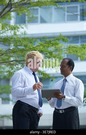 Indian and caucasian businessmen discussing work using digital tablet while standing outdoors Stock Photo