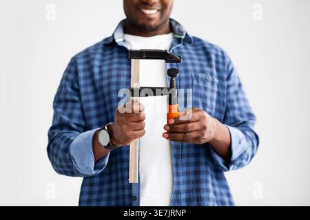 Cropped image of Black man holding clamp tool standing against white wall at home Stock Photo