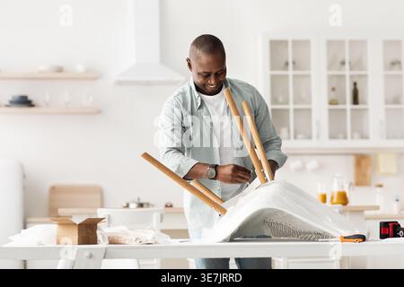 Black man assembling chair standing in kitchen at home Stock Photo