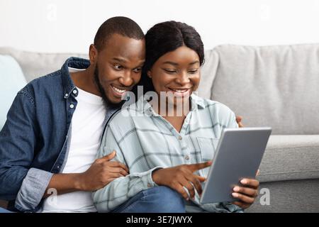 Black husband and wife using tablet while sitting together on floor in living room at home Stock Photo
