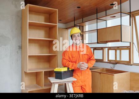 Asian male construction worker wearing safety helmet leaning arm on toolbox while standing in construction site Stock Photo