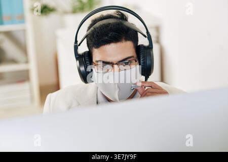 Indian male customer service employee with headphones answering calls while working in office Stock Photo