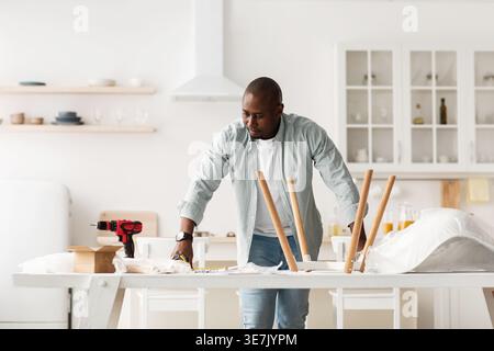 Black man reading instructions on assembling chair standing at table in kitchen at home Stock Photo