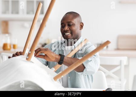 Black man assembling chair standing in kitchen at home Stock Photo
